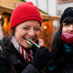 Two women at a Christmas market eating apple and candy in front of a booth.